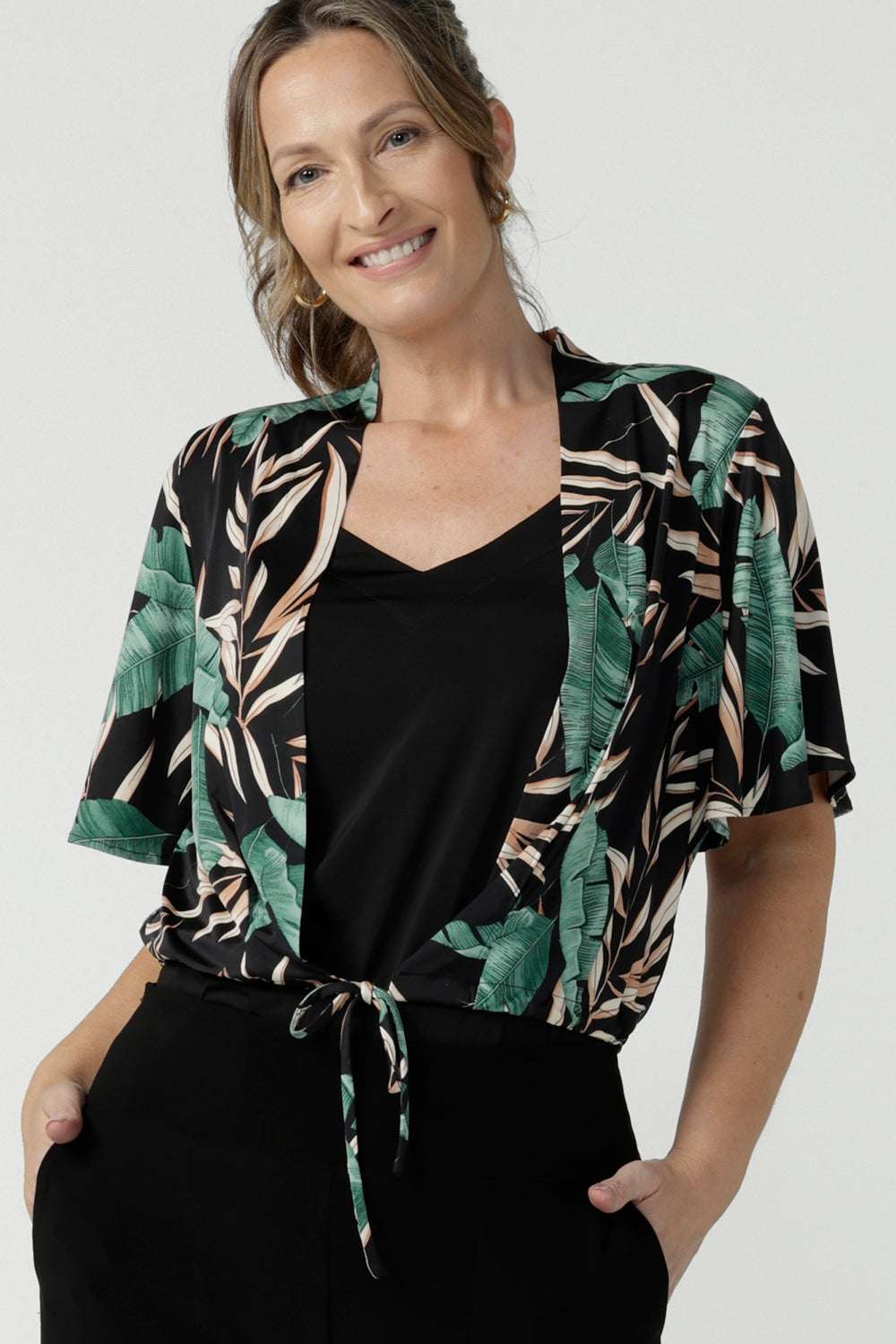 Tropical printed shrug cardigan. Featuring a leaf print on a black background. Ruched waist tie detail tie detail. Great layering piece. Ladies inclusive sizing. Size 8 pictured.