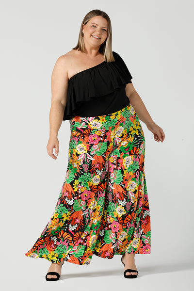 A curvy size 18 woman wears the Caspian Palazzo pant in a beautiful bright colourful print. In soft and lightweight jersey this pant features side pocket and a wide leg opening. Styled back with a black off shoulder top and black heels. Made in Australia size 8-24.