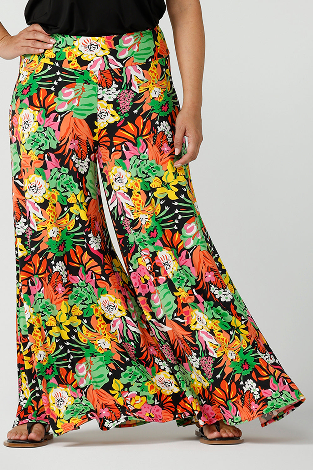 Close up of a size 12 woman wearing the Caspian Palazzo pant n a beautiful bright colourful print. In soft and lightweight jersey this pant features side pocket and a wide leg opening. Styled back with a black cami top and flat sandals. A perfect look for weekend wear. Made in Australia size 8-24.