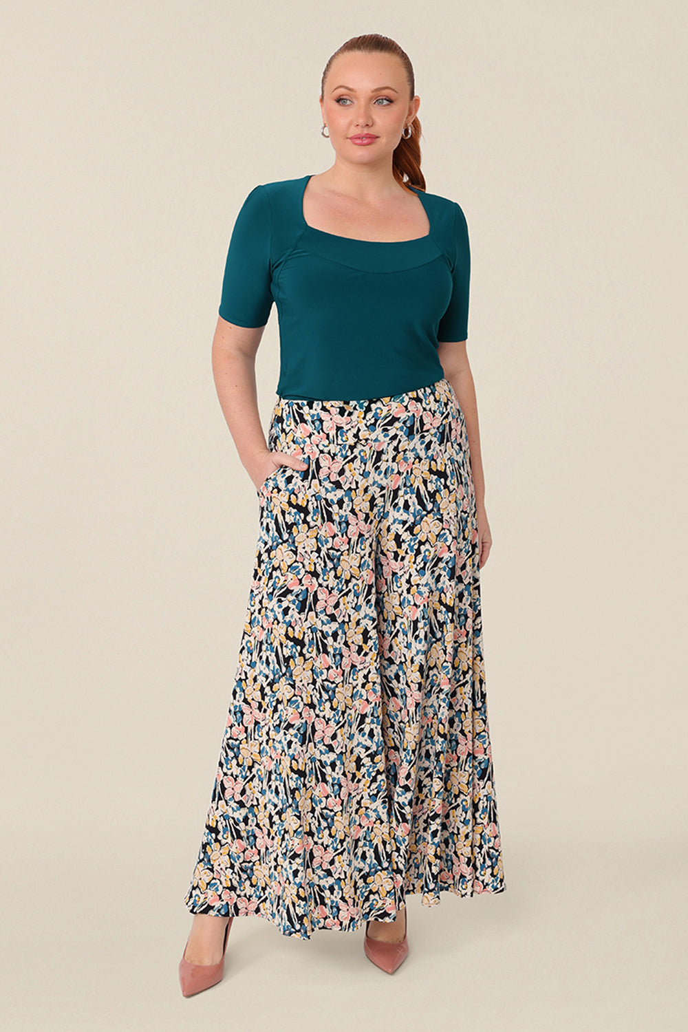 A curvy size, size 12 woman wears printed wide leg pants with pockets with a square neck dark teal top. These pull-on, easy care pants are comfortable for your everyday workwear capsule wardrobe. Shop these Australian-made wide leg trousers online in sizes 8 to 24, petite to plus sizes.