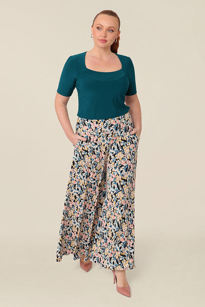 A fuller figure, size 12 woman wears floral printed wide leg pants with pockets and square neck, dark teal top as a casual outfit. These pull-on, easy care pants are comfortable for your everyday capsule wardrobe. Shop these Australian-made wide leg trousers online in sizes 8 to 24, petite to plus sizes.