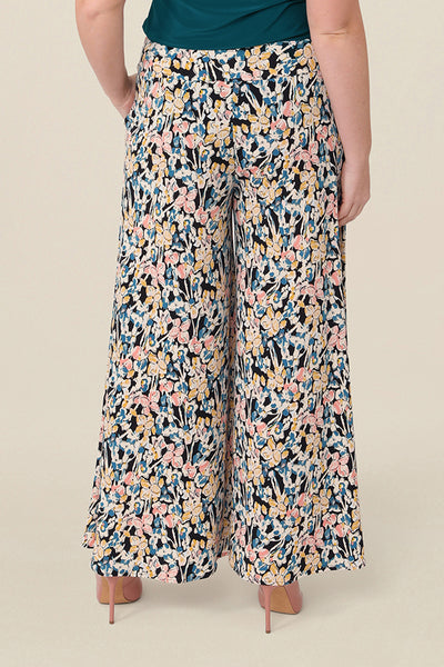 Back view of a curvy size, size 12 woman wearing floral printed wide leg pants with pockets. These pull-on, easy care pants are comfortable for your everyday capsule wardrobe. Shop these Australian-made wide leg trousers online in sizes 8 to 24, petite to plus sizes.