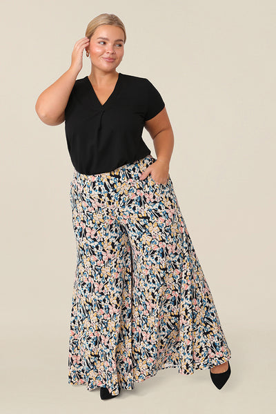 A petite height, size 16 woman wears floral printed wide leg pants with pockets. These pull-on, easy care pants are comfortable for your everyday capsule wardrobe. Shop these Australian-made wide leg trousers online in sizes 8 to 24, petite to plus sizes.
