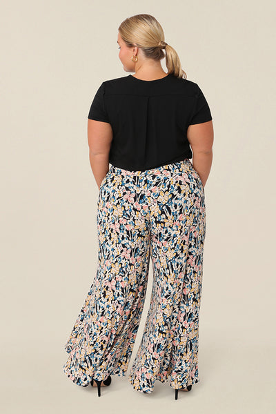 Back view of a petite height, size 16 woman wearing floral printed wide leg pants with pockets. These pull-on, easy care pants are comfortable for your everyday capsule wardrobe. Shop these Australian-made wide leg trousers online in sizes 8 to 24, petite to plus sizes.