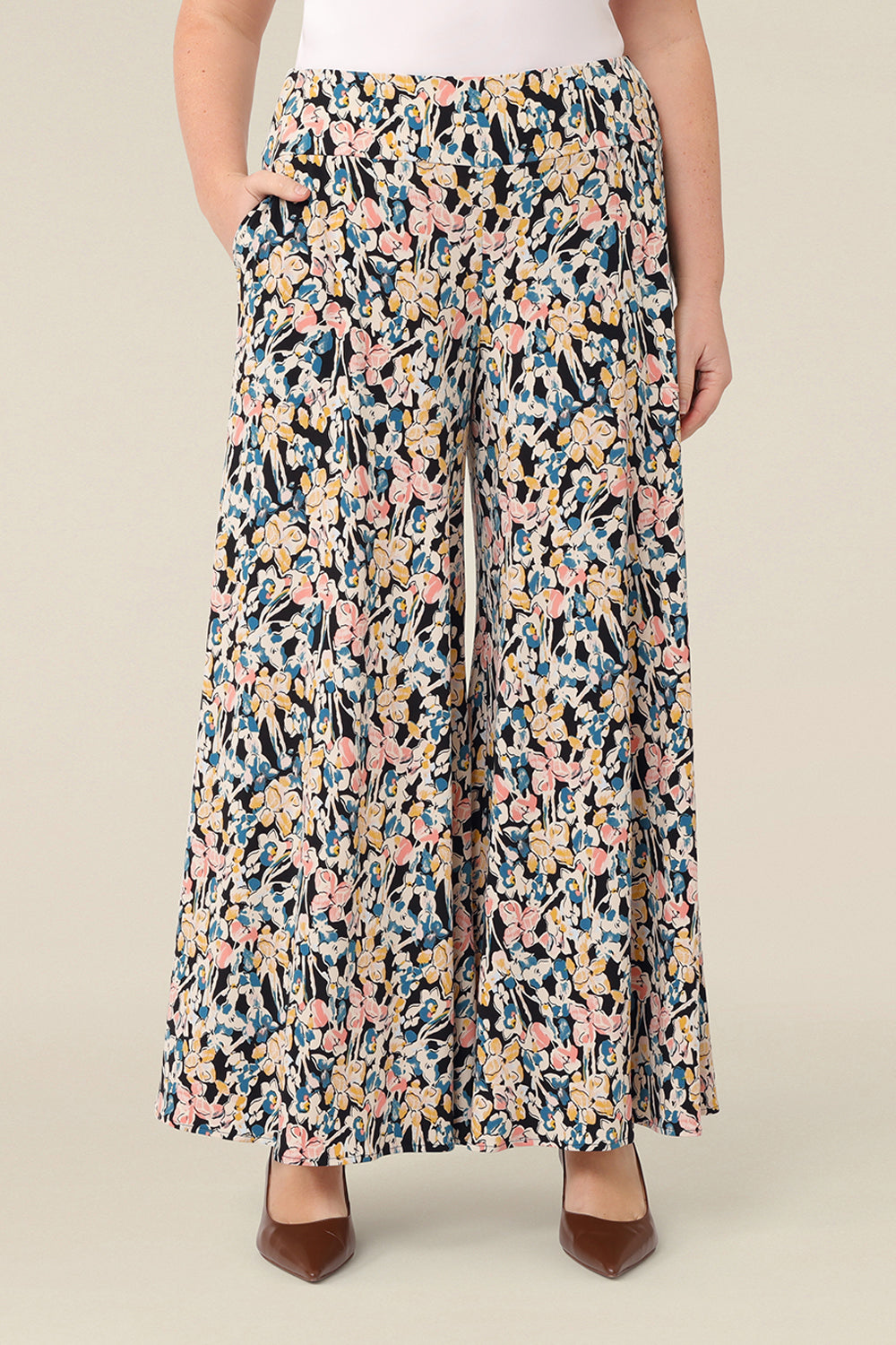 A curvy size, size 12 woman wears floral printed wide leg pants with pockets. These pull-on, easy care pants are comfortable for your everyday capsule wardrobe. Shop these Australian-made wide leg trousers online in sizes 8 to 24, petite to plus sizes.