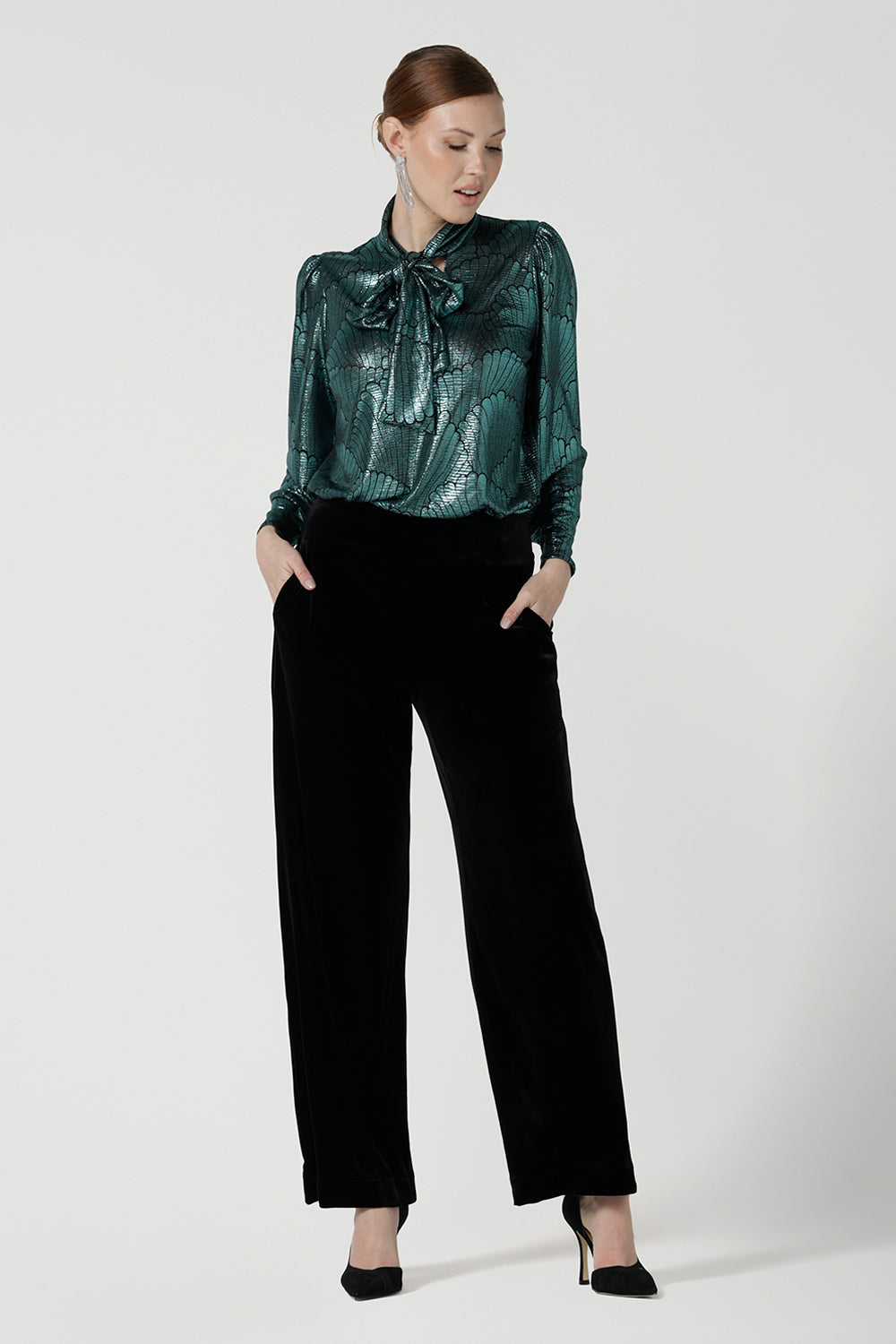 Size 10 woman wears the Celine top in Mikado Green, a tie neck top with a cuffed sleeve. Made in Australia for women size 8 - 24. Styled back with Black Deni pants in Velour. 