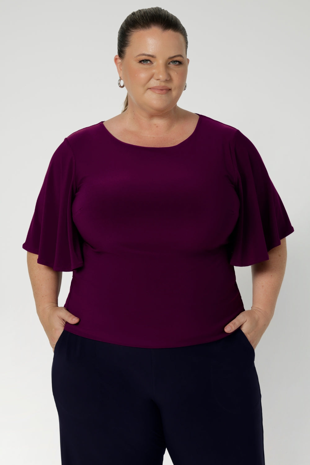 Plus size woman wears a workwear top with elbow-length flutter sleeves that offer a graceful, feminine finish, while the double-layer bodice ensures a flattering, smooth silhouette. With a straight hemline, this top is easy to tuck into skirts or trousers, making it a versatile piece for the corporate woman on the go. 