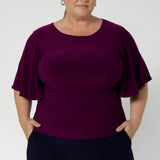 Plus size woman wears a workwear top with elbow-length flutter sleeves that offer a graceful, feminine finish, while the double-layer bodice ensures a flattering, smooth silhouette. With a straight hemline, this top is easy to tuck into skirts or trousers, making it a versatile piece for the corporate woman on the go. 