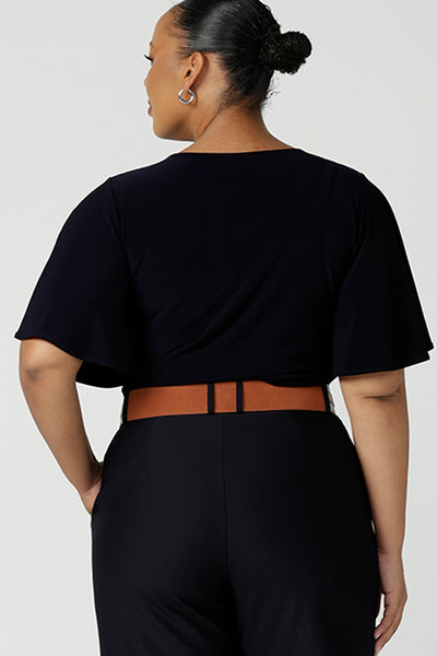 Back view of A plus size 18 woman wears a casual jersey top in navy blue, styled with navy tailored pants. This Australian-made women's top has flutter sleeves, a high, round neckline and and high-low hem perfect for weekend casual and travel capsule wardrobes.