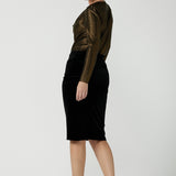 Woman wears the Brooke Skirt in Black Velour. Slim fit tube skirt for evening wear. Flattering style. Size inclusive fashion Australian made size 8 - 24. Styled back with black high heel and cowl neck gold Chrissy Top.