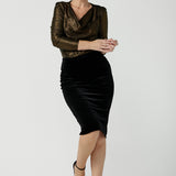 Woman wears the Brooke Skirt in Black Velour. Slim fit tube skirt for evening wear. Flattering style. Size inclusive fashion Australian made size 8 - 24. Styled back with black high heel and cowl neck gold Chrissy Top. 