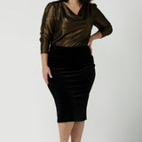 Woman wears the Brooke Skirt in Black Velour. Slim fit tube skirt for evening wear. Flattering style. Size inclusive fashion Australian made size 8 - 24. Styled back with black high heel and cowl neck gold Chrissy Top.