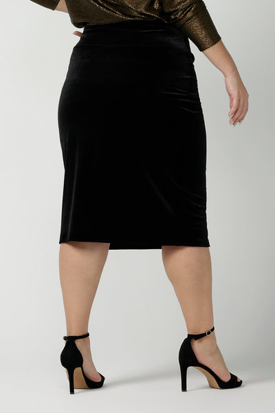 Back view of a Woman wears the Brooke Skirt in Black Velour. Slim fit tube skirt for evening wear. Flattering style. Size inclusive fashion Australian made size 8 - 24. Styled back with black high heel and cowl neck gold Chrissy Top.