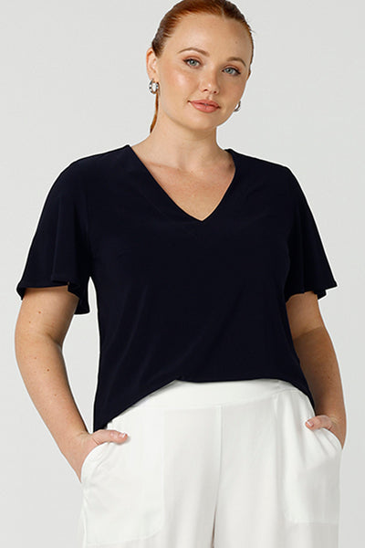 Worn by a size 12, curvy woman, this is a semi-fitted, V-neck top with flutter sleeves in navy blue jersey. Made in Australia by women's clothing brand, Leina & Fleur , this  classic top is great for capsule wardrobes, smart casual wear and as a work blouse. Shop women's clothing online in sizes 8 to 24 at L&F's online fashion boutique!