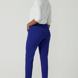 Back view of a  size 10 woman wears the Corbin Pant in Cobalt, a high waist pant with belt loops and cropped leg length. Made in Australia for women size 8-24. Comfortable cocktail suiting work suit look for corporate women. Size inclusive petite to plus size fashion 8-24.