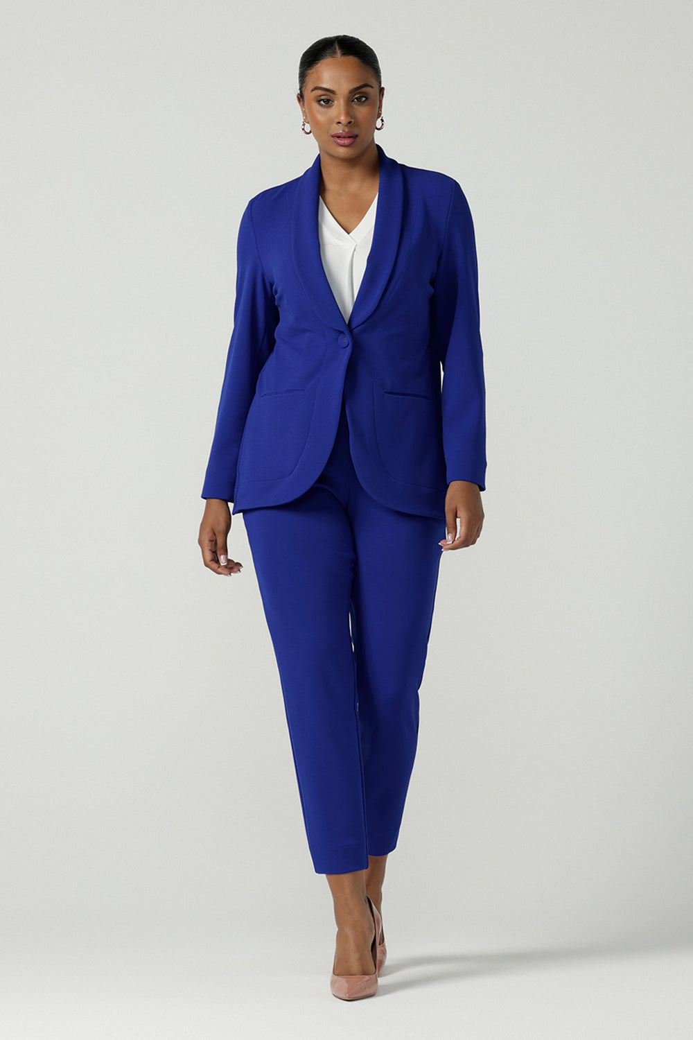 A size 10 woman wears the Corbin Pant in Cobalt, a high waist pant with belt loops and cropped leg length. Made in Australia for women size 8-24. Comfortable cocktail suiting work suit look for corporate women. Size inclusive petite to plus size fashion 8-24. Styled back with the Merit Blazer in Cobalt. 