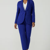 A size 10 woman wears the Corbin Pant in Cobalt, a high waist pant with belt loops and cropped leg length. Made in Australia for women size 8-24. Comfortable cocktail suiting work suit look for corporate women. Size inclusive petite to plus size fashion 8-24. Styled back with the Merit Blazer in Cobalt. 