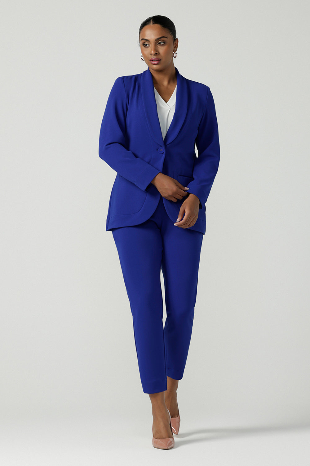 A size 10 woman wears the Corbin Pant in Cobalt, a high waist pant with belt loops and cropped leg length. Made in Australia for women size 8-24. Comfortable cocktail suiting work suit look for corporate women. Size inclusive petite to plus size fashion 8-24. Styled back with the Merit Blazer in Cobalt.