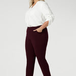 The invisible front zip with an internal button ensures a sleek, clean look while providing a secure fit. Size 18 woman wears her Corbin Pants with white blouse and brown heels.