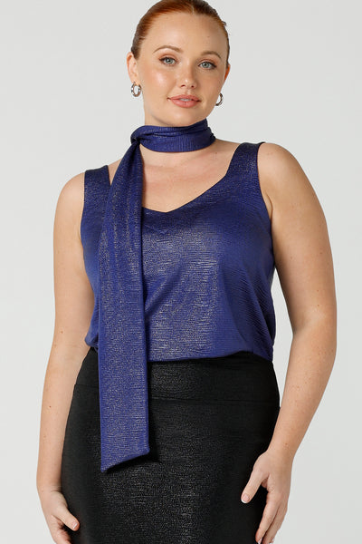 A size 12, fuller figure woman wears a cobalt Xanadu cami top with wide shoulder straps. Made in Australia by Australian and New Zealand women's clothing company. She wears this shimmer jersey top with a matching neck tie. 