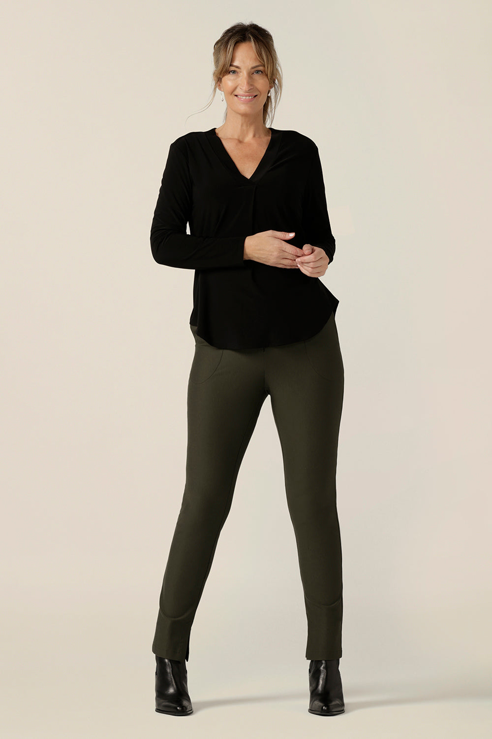 A size 10, 40 plus woman wears a long sleeve top with V-neck in black jersey with slim leg Olive green pants. Made in Australia by Australian and New Zealand women's clothing label, L&F .