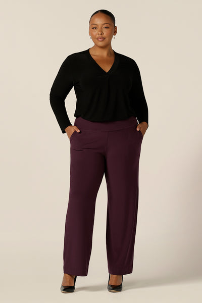 A plus size, size 18 woman wears a long sleeve top with V-neck in black jersey worn with straight, wide leg trousers in Mulberry. Made in Australia by Australian and New Zealand women's clothing label, L&F .