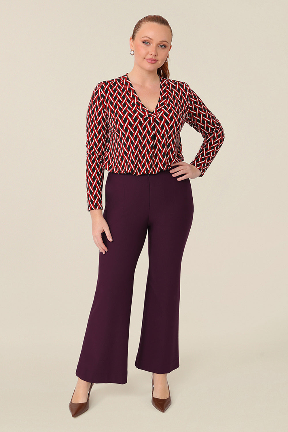 A long sleeve, women's work top, this red, white and black chevron print V-neck top has a shirttail hem. Worn with mulberry red tailored work pants with flared legs. Shop this office top at Australian fashion brand, L&F in petite to plus sizes.