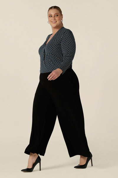 A plus size woman wears black wide leg pants with pockets and a V-neck, long sleeve work top to wear at the office. These pull-on, easy care pants are comfortable for your everyday workwear capsule wardrobe. Shop these stretchy  jersey black pants online in sizes 8 to 24, petite to plus sizes.