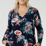The floral pattern, highlighted in soft shades of pink, red, and blue, adds a timeless feminine touch while the stretch-infused fabric ensures all-day comfort and ease of movement. Plus size woman wears her untucked over navy stretchy pants for women.