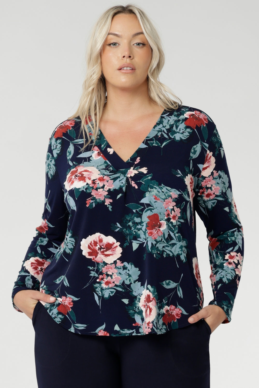 The floral pattern, highlighted in soft shades of pink, red, and blue, adds a timeless feminine touch while the stretch-infused fabric ensures all-day comfort and ease of movement. Plus size woman wears her untucked over navy stretchy pants for women.