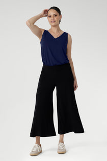 A size 10 woman wears black wide-leg pants and navy top. Cropped in length, the black pants have a smooth waistband, side pockets and are pull-on pants made in stretch jersey. Made in Australia, the pants are size inclusive in sizes 8 - 24.