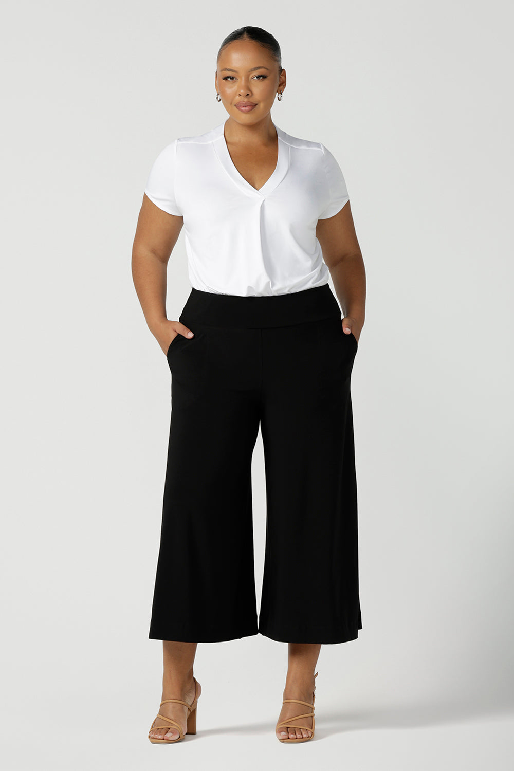 A size 18, plus size size woman wears a short sleeve, V neck top in white bamboo jersey with wide leg, black culotte pants. A great top for plus size women, the tailored pleat below the V neckline flatters curves. Shop tops made in Australia at women's clothing brand, Leina & Fleur.