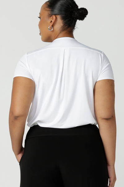 Back view of a size 18, plus size size woman wearing a short sleeve, V neck top in white bamboo jersey. A great top for plus size women, the tailored pleat below the V neckline flatters curves. Shop tops made in Australia at women's clothing brand, Leina & Fleur.