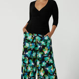 A size 10 woman wears the Dany culotte in Canopy, a full leg culotte with a canopy print. A bold green colour splatter print. Styled back with pink heels and a navy wrap top. Made in Australia for women size 8 - 24.