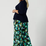 Back view of a size 18 woman wears the Dany culotte in Canopy, a full leg culotte with a canopy print. A bold green colour splatter print. Styled back with pink heels and a navy wrap top. Made in Australia for women size 8 - 24.