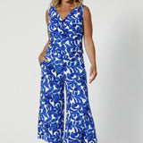 Size 12 woman wears wide leg printed pants made with lightweight dry-touch jersey with print details in shades of blue leaves. Summer ready pants have been styles with matching sleeveless top for a faux jumpsuit look, paired with tall silver heels for an elevated look for summer outings.