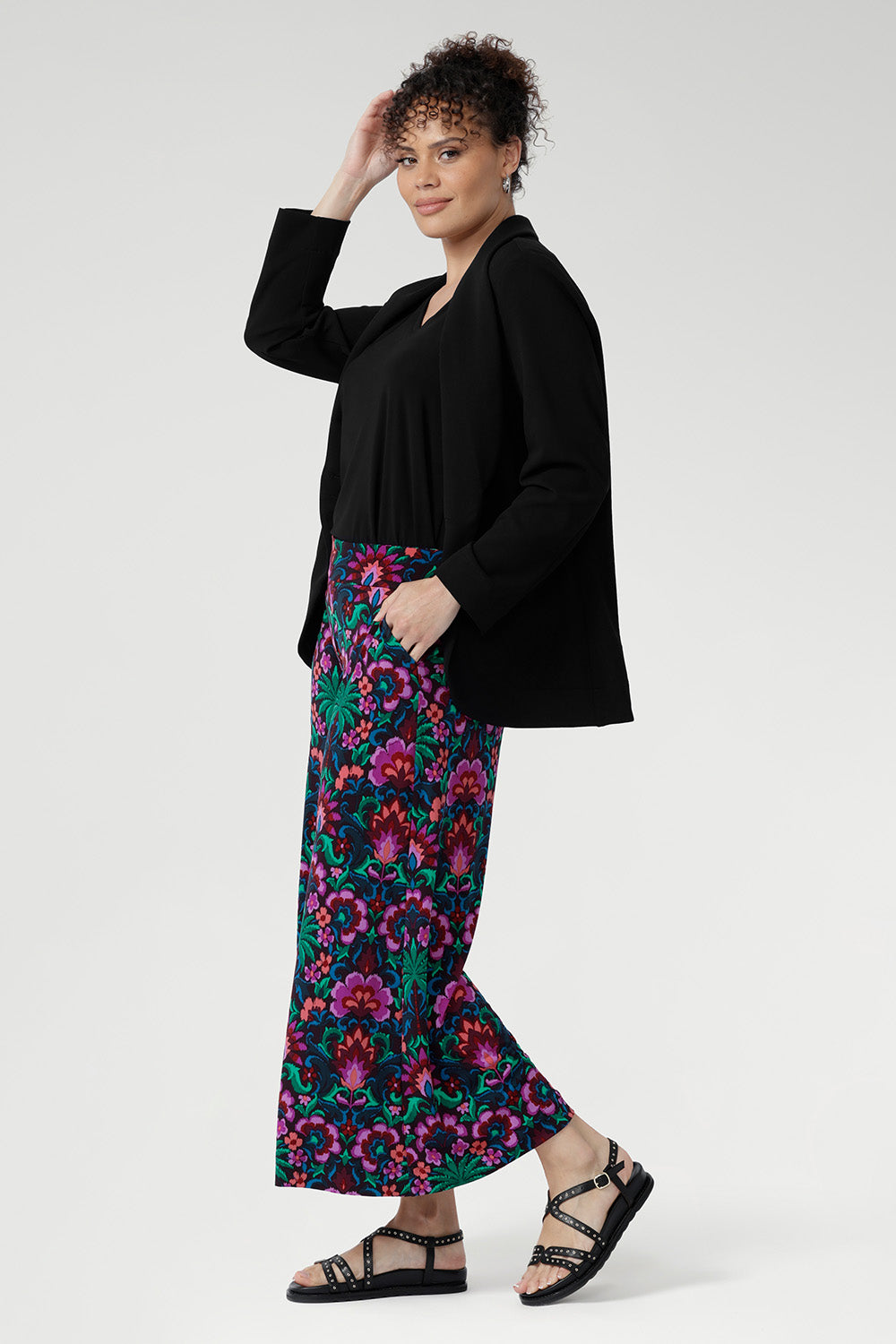 Over 30's woman wearing a black blazer and colourful floral culottes with chunky black sandals. Designed with an extra-wide leg and cropped length, it offers a relaxed yet elevated silhouette that transitions effortlessly from casual daywear to evening style.