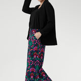 Over 30's woman wearing a black blazer and colourful floral culottes with chunky black sandals. Designed with an extra-wide leg and cropped length, it offers a relaxed yet elevated silhouette that transitions effortlessly from casual daywear to evening style.