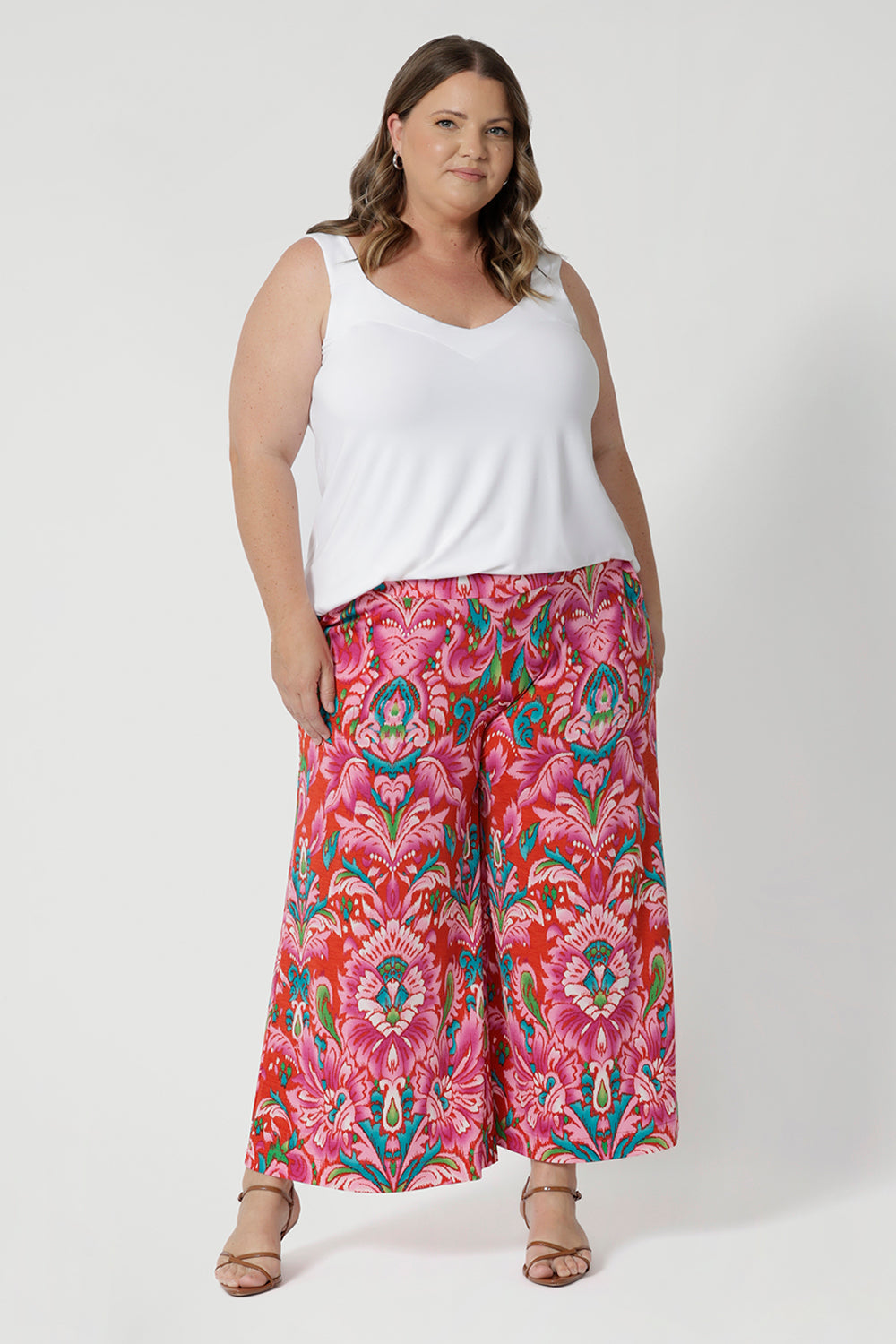 Plus sized woman wears cropped printed pants with summer cami in white to tie in with all the bold colours showcased in the print. Made from lightweight crepe jersey fabric, they offer cool and comfortable qualities making them ideal for travel. The jersey fabric’s stretch appeal is ideal for everyday comfort and style. Proudly stocked in sizes 8-24.