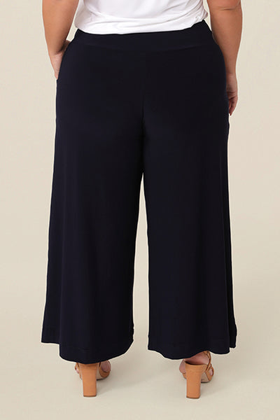 Back view of good pants for petite women. A curvy, size 16 woman wears black culotte pants by Australian fashion brand, Leina & Fleur. Cropped trousers with a stretchy, pull on waistband, these easy-care wide leg pants are worn with a short sleeve top in white bamboo jersey.