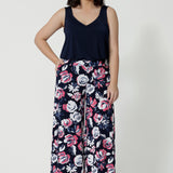 Full body image of a petite woman wearing a light weight pair of floral printed pants. The floral design has navy, pink and white roses. This Australian made pant is made from dry touch jersey fabric. Breathable and easy care pant is comfortable and can be worn casually and or dressed up. Leina & Fleur is a women’s clothing company that actively stocks plus sizes & petite sizes ranging from 8 to 24.