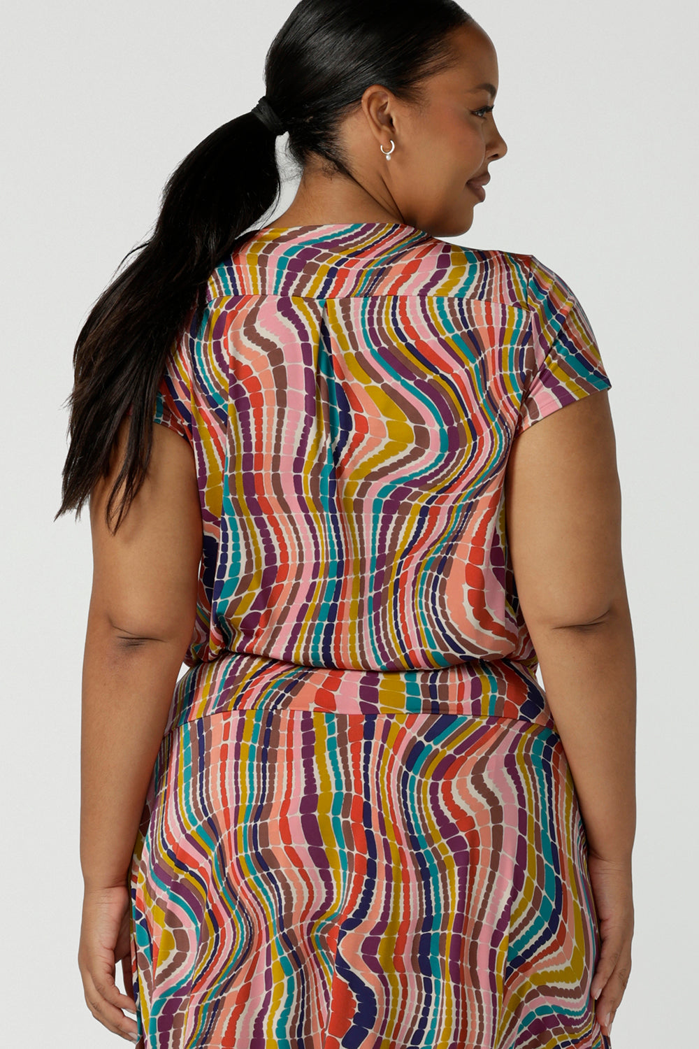 Back view of a curvy size 16 woman wears the Daryl Top in Kaleidoscope. A cowl neck style top with rainbow stripes and slinky. Styled back with the Berit Maxi skirt. Soft Slinky jersey made in Australia for women in size 8 - 24.