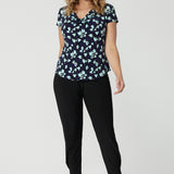 Showing a good summer top for women, an over 40s woman wears a cowl neck top in aqua blue floral print. This short sleeve top for women is worn with tapered leg, black travel pants and sneakers. This casual top is made in Australia by Australian and New Zealand women's clothes brand, Leina & Fleur.