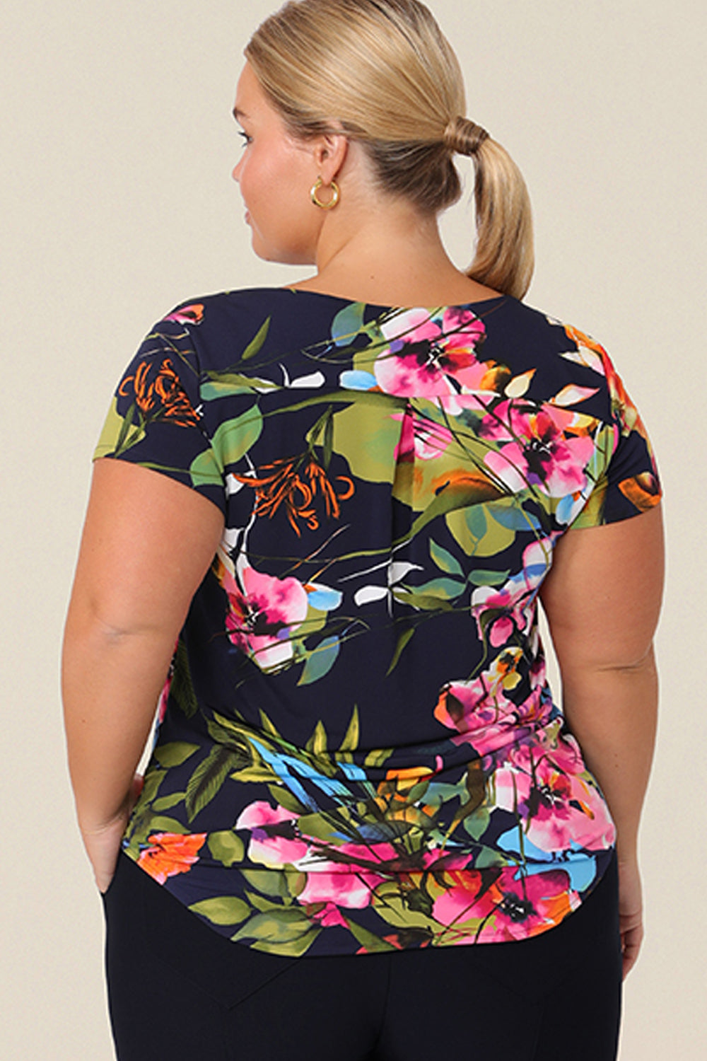 Back view of a size 14 curvy woman wears a cowl neck short sleeve jersey top in a floral print. She wears the top with work trousers in navy. Both are designed and made in Australia for petite to plus size women.