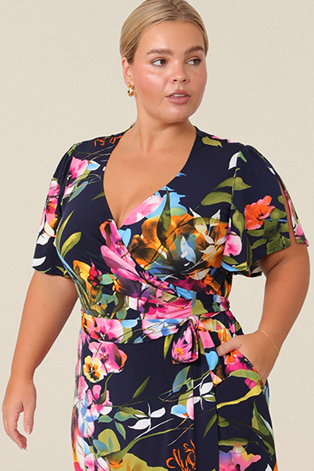 A size 14 petite height woman wears a functioning wrap dress with peekaboo flutter sleeves. Featuring a midi-length skirt with wrap hem, this floral printed jersey dress is has a v-neckline and wears well as an everyday dress. 