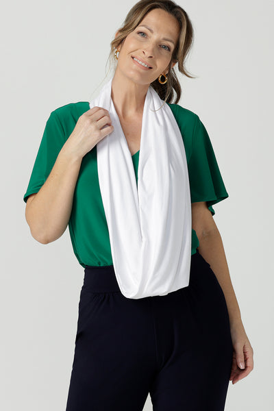 A 40 plus woman wears an infinity scarf in white bamboo jersey over a green flutter sleeve jersey top and dropped crotch pants for travel wear.