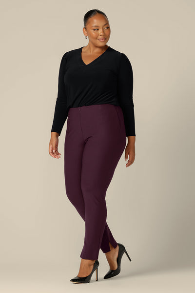 A size 18, plus size woman wears mid-rise, slim leg pants in mulberry ponte jersey by Australia and New Zealand women's clothing brand, L&F. Good pants for work, these comfortable trousers are worn with a long sleeve, V-neck top in black jersey.