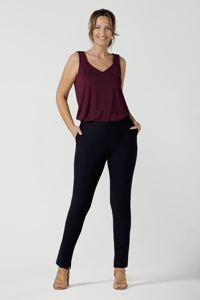 A size 10, 40 plus woman wears mid-rise, slim leg navy pants by Australian and New Zealand women's clothing label, L&F. These skinny workwear trousers have a concealed zip fastening and side pockets. Worn with a plus red cami top with wide shoulder straps. Shop these navy workwear pants in an inclusive size range of 8 to 24.