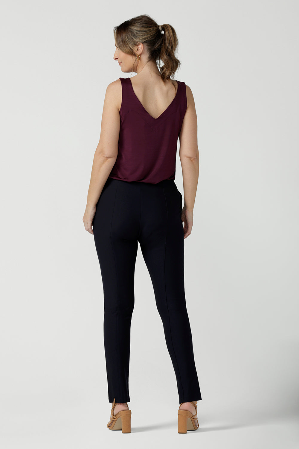 Back view of a size 10, 40 plus woman wearing mid-rise, slim leg navy pants by Australian and New Zealand women's clothing label, L&F. These skinny workwear trousers have a concealed zip fastening and side pockets. Worn with a plus red cami top with wide shoulder straps. Shop these navy workwear pants in an inclusive size range of 8 to 24.