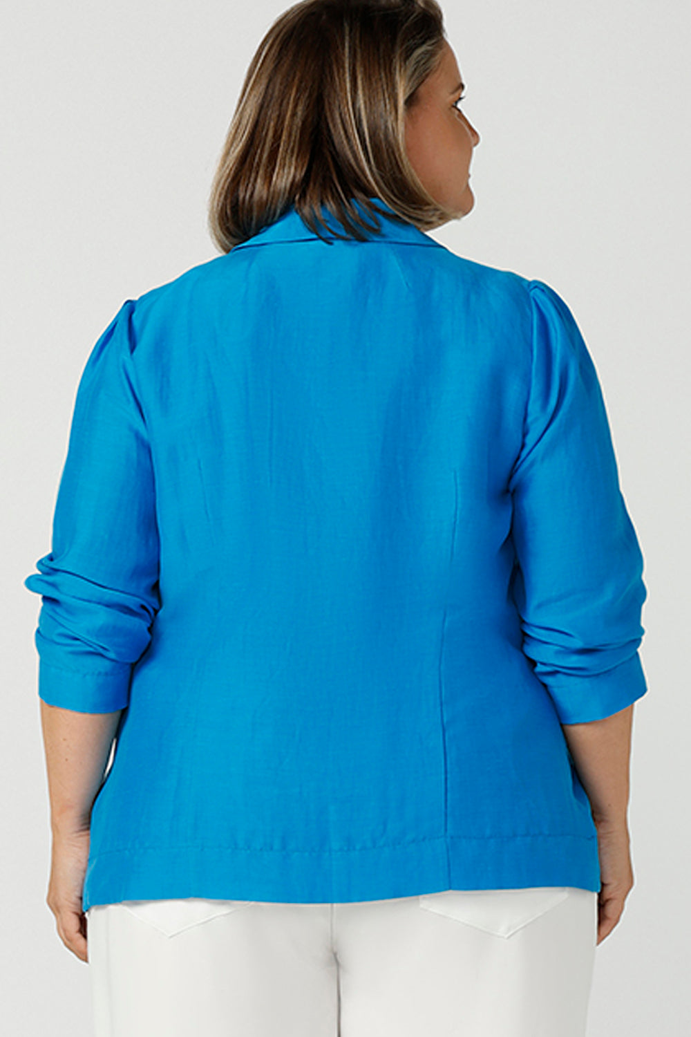 Back view of A curvy size, size 16 woman wearing a longline blazer in opal blue tencel fabric with a white bamboo cami. This lightweight jacket is comfortable for your everyday workwear, casual and travel capsule wardrobe. Shop this Australian-made blazer online in sizes 8 to 24, petite to plus sizes.